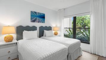 A hotel room with two beds, a large window with curtains, a wall-mounted painting, and bedside lamps.