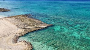 Una zona costera con aguas turquesas cristalinas, una playa rocosa y un muelle que se adentra en el mar.