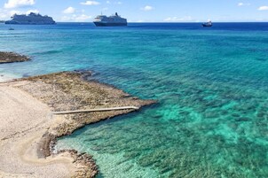 Uma área costeira com águas turquesa cristalinas, uma praia de pedras e um cais que se estende para o mar.
