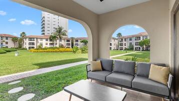 Un área de estar moderna al aire libre con un sofá y una mesa, con vistas a un césped cuidado y un conjunto de edificios.