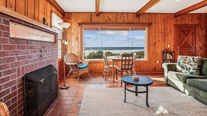 Una habitación acogedora con chimenea, sillones de mimbre, una mesa redonda y vista al océano.