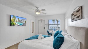 Ein Hotelzimmer mit Bett, Deckenventilator, Fenster mit Ausblick und einem gerahmten Bild an der Wand.