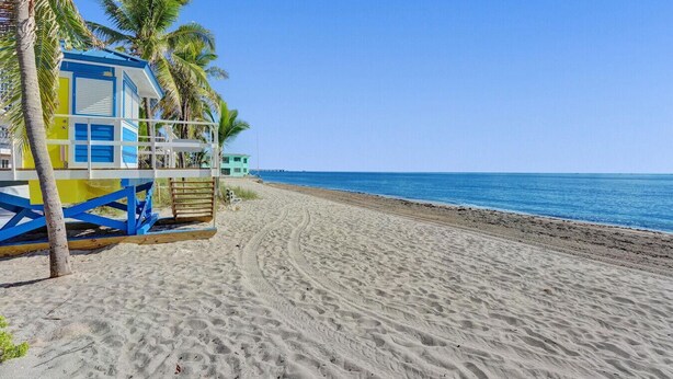 Ein Strand mit einem Rettungsturm, Palmen und blauem Himmel.