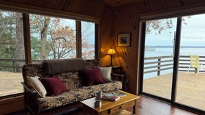 Een gezellig interieur van een chalet, met een bank, een tafel en uitzicht op een houten terras en water.