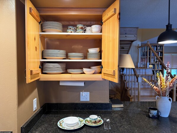 A kitchen with wooden cabinets, a marble countertop, and a dining area with a vase of dried flowers. - Gorgeous Lake Eau Claire home! (Augusta)