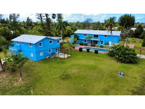 Ein großes blaues Haus mit Schwimmbad, umgeben von üppiger Vegetation und Palmen.