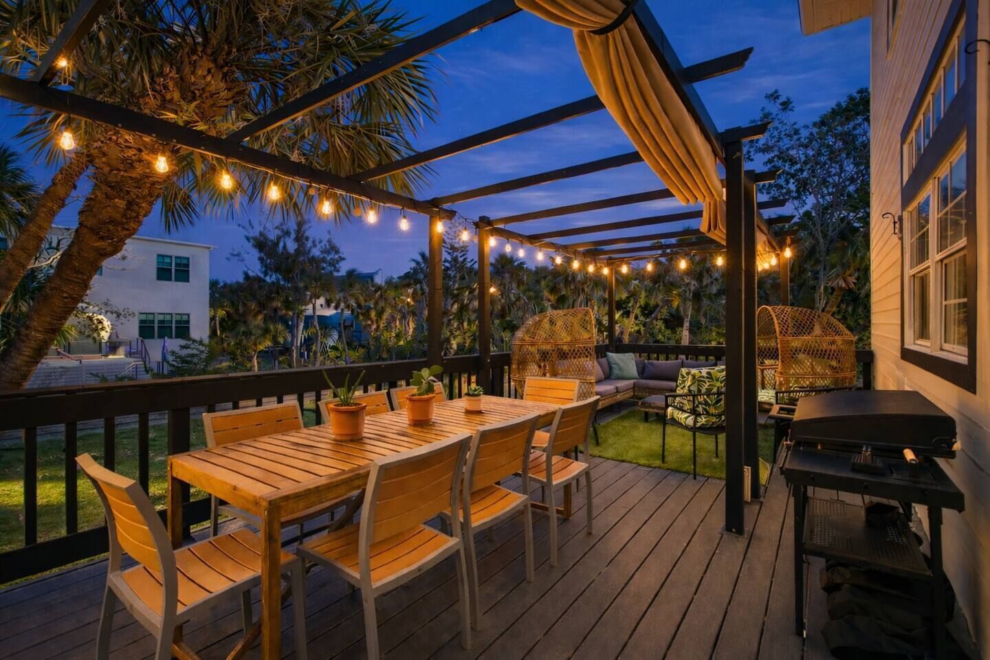 An outdoor deck with a wooden table and chairs, string lights, and a grill.