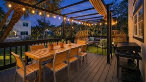 An outdoor deck with a wooden table and chairs, string lights, and a grill. - Siesta Key Pool House with Fire Pit & Deck (Sarasota)