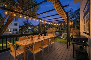 An outdoor deck with a wooden table and chairs, string lights, and a grill. - Siesta Key Pool House with Fire Pit & Deck (Sarasota)