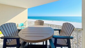Un balcón con una mesa y dos sillas Adirondack con vista a la playa.