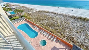 Zona de piscina con un pequeño jacuzzi, rodeada de sillas de descanso, con vistas a una playa.