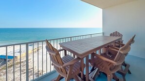 Una mesa y sillas de madera en un balcón con vista a la playa y el océano.