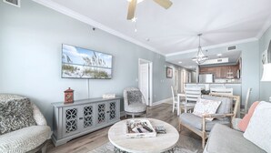 Una sala de estar con televisión, asientos, un comedor y una cocina al fondo.
