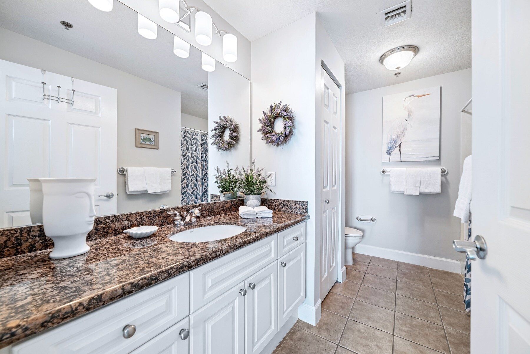 A bathroom with a granite countertop, two sinks, a toilet, and a shower.