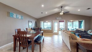 A spacious living room with a large sofa, a dining area with wooden furniture, and a ceiling fan. - Waterfront Home on Lake Limestone w/ Dock (Groesbeck)