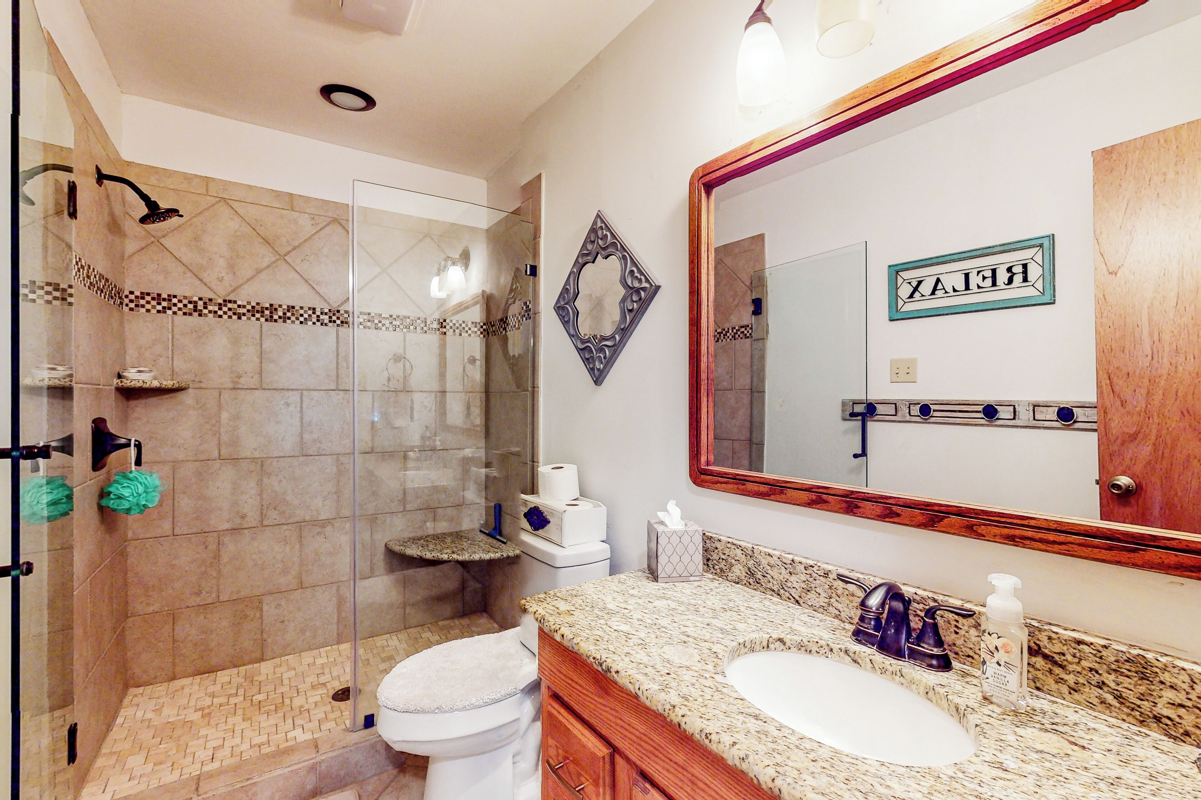 A bathroom with a glass-enclosed shower, a toilet, a sink with a marble countertop, and a large mirror with a 'RELAX' sign.
