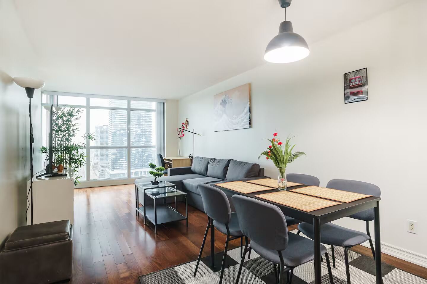 Un salon moderne comprenant un canapé, une table à manger, des chaises et une grande fenêtre donnant sur la ville.