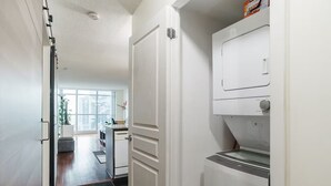 A laundry room with a washing machine and dryer, a door leading to a living area, and a view of a cityscape through large windows.