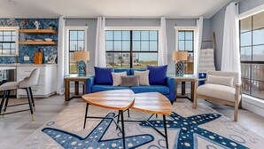A modern living room with a blue sofa, two wooden side tables, and a star-patterned rug. - Walk to Beach! Updated Home in South Padre Island (South Padre Island)