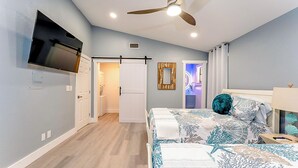 A bedroom with a bed, a ceiling fan, a TV mounted on the wall, and a bathroom door. - Walk to Beach! Updated Home in South Padre Island (South Padre Island)
