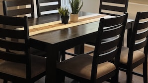 Comedor con mesa de madera oscura, seis sillas, una planta en maceta y un adorno de bicicleta colgada en la pared.