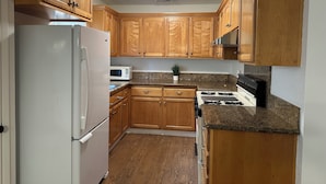 Una cocina con armarios de madera, un refrigerador blanco, un microondas, una estufa y encimeras de granito.
