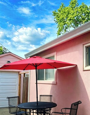Uma casa rosa com garagem, uma janela e um pátio com mesa e cadeiras.