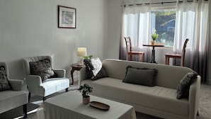 Sala de estar con sofá, sillones, una mesa de centro, una mesita auxiliar con lámpara y una ventana con cortinas.