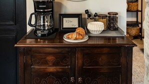 A wall-mounted clock, a coffee maker, a framed picture, and a plate with croissants on a wooden cabinet. - Charming 2BR Cottage · Near Lake Lookout · Wine Tasting Included · Pet Friendly (Portland)