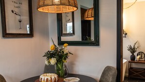 A dining area with a round table, two chairs, a wicker pendant light, a vase with flowers, and framed artwork on the wall. - Charming 2BR Cottage · Near Lake Lookout · Wine Tasting Included · Pet Friendly (Portland)