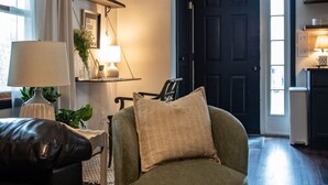 A living room with a green armchair, a brown leather sofa, a lamp, a plant, and a door in the background. - Charming 2BR Cottage · Near Lake Lookout · Wine Tasting Included · Pet Friendly (Portland)