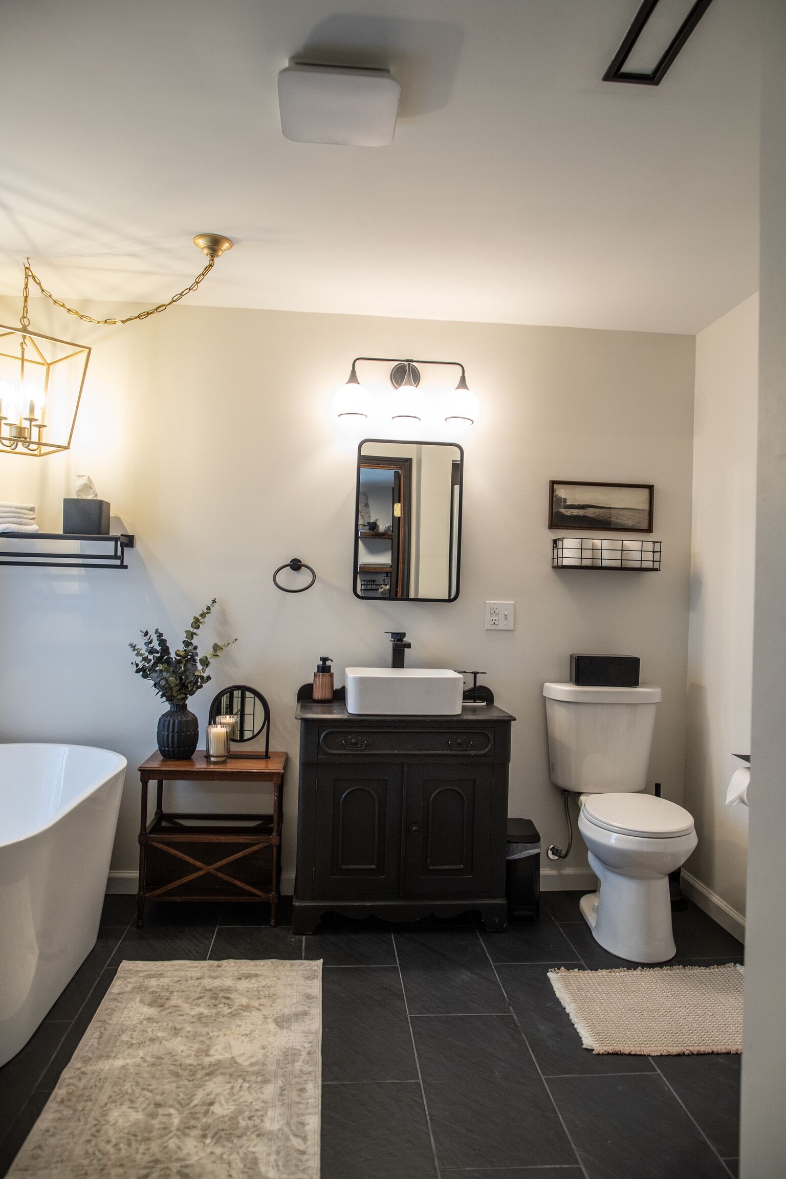 A bathroom with a freestanding bathtub, a vanity with a mirror, a toilet, and a rug on the floor.