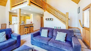 A spacious living area with a wooden staircase, a kitchen in the background, and a cozy seating arrangement. - Gateway to Crater Lake! Resort Retreat w/ Pool (Klamath Falls)