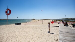 Ein Strand mit einem Rettungsring, einer Holzstege und Menschen, die verschiedene Aktivitäten ausüben.