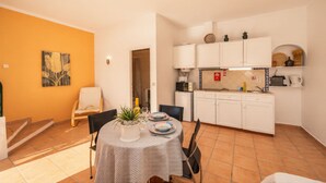 Een compacte keuken met witte kastjes, een eettafel met stoelen en een kleine potplant.
