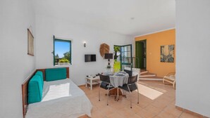 Een moderne slaapkamer met een bed, een bureau en een stoel. Er is een televisie aan de muur en een raam met uitzicht op groen.