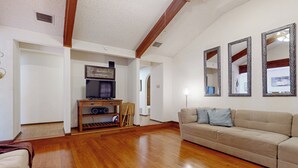 Un soggiorno con pavimento in legno, un divano beige e una televisione su un supporto in legno.