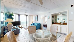Ein modernes Wohnzimmer mit einem Glastisch, Korbstühlen, einem blauen Sofa und einem Flachbildfernseher.