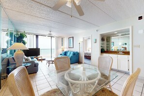 A modern living room with a glass coffee table, wicker chairs, a blue sofa, and a flat-screen TV. - Coastal Chic Gulf-View 2BR: Suntide III - Unit 604 (South Padre Island)