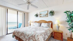 Ein Schlafzimmer mit einem großen Bett, zwei Nachttischen mit Lampen, einem Deckenventilator, einem Balkon mit Stuhl und einem Blumentopf.