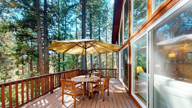 Un patio in legno con tavolo e sedie, circondato da alberi alti.