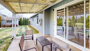 A covered patio with a table and chairs, a grassy yard, and a house with a sliding glass door. - Tranquil Redmond Retreat: Relax & Explore Outdoors (Redmond)