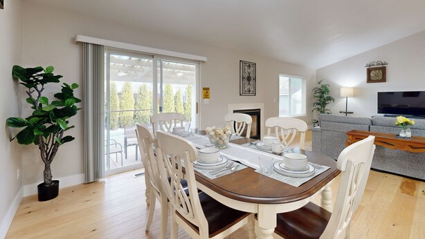 A dining area with a wooden table set for four, surrounded by white chairs. There is a potted plant to the left and a sofa in the background. - Tranquil Redmond Retreat: Relax & Explore Outdoors (Redmond)