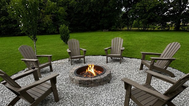 A circular outdoor seating area with four Adirondack chairs around a stone fire pit.