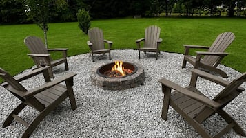 Un espace extérieur circulaire aménagé avec des sièges et quatre fauteuils Adirondack disposés autour d’un foyer en pierre.