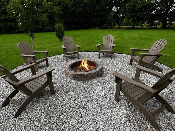 A circular outdoor seating area with four Adirondack chairs around a stone fire pit.