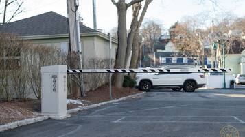 A gated driveway with a white SUV parked inside, a security box, and a no-entry sign.
