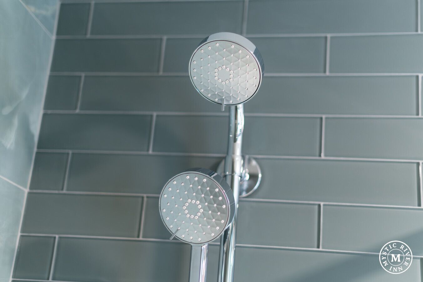 A shower with two round, perforated heads mounted on a chrome fixture.