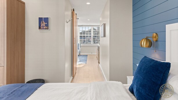 A bedroom with a bed, a blue accent wall, a wooden wardrobe, and a view of a balcony.