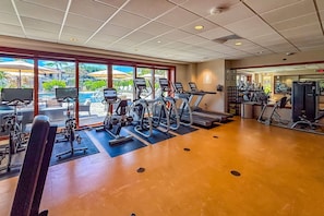 A gym with cardio machines, weight equipment, and a view of a pool and greenery. - Wailea Beach | Oceanfront 6 BR, Sleeps 12 | Car Incl. w/ 6+ Nights | WBV ML-3485 by KBM (Wailea)